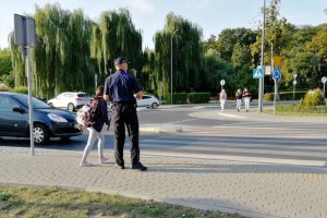 Policjant pomaga dziecku przejść przez jezdnię