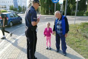 Policjant wręcza dziewczynce odblaskowa opaskę