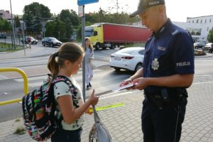 Funkcjonariusz przekazuje opaskę odblaskową dziewczynce