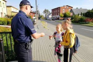 Policjant rozmawia z uczennicami szkoły o zasadach obowiązujących w rejonie szkoły