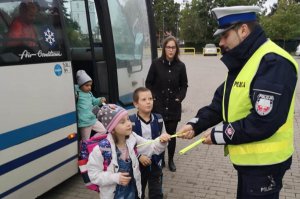 Policjant ruchu drogowego wręcza dzieciom opaski odblaskowe