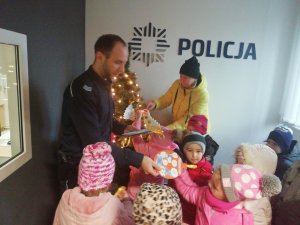 Policjant wręcza dekoracje dzieciom stojącym obok choinki