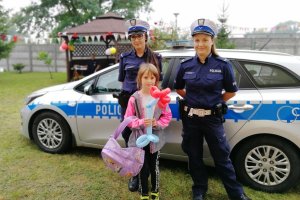 Policjantki drogówki stoją z dziewczynką na tle radiowozu