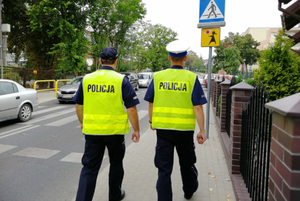 Policjanci idący chodnikiem w rejonie przejścia dla pieszych