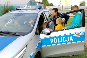 Policjantka ruchu drogowego pokazuje grupie dzieci radiowóz oznakowany