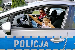 Dziewczynka siedząc na miejscu kierowcy w radiowozie pokazuje kciuka
