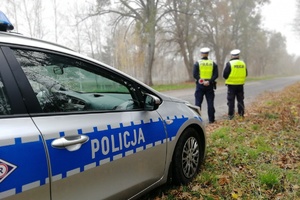 Jesienna pogoda, policjanci kontrolują ruch pojazdów stojąc obok radiowozu