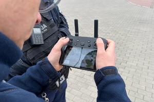 Policjant trzyma w ręku aparaturę sterującą dronem
