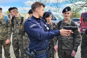 Policjant trzem w ręku broń krótką i prezentuje ją uczniom